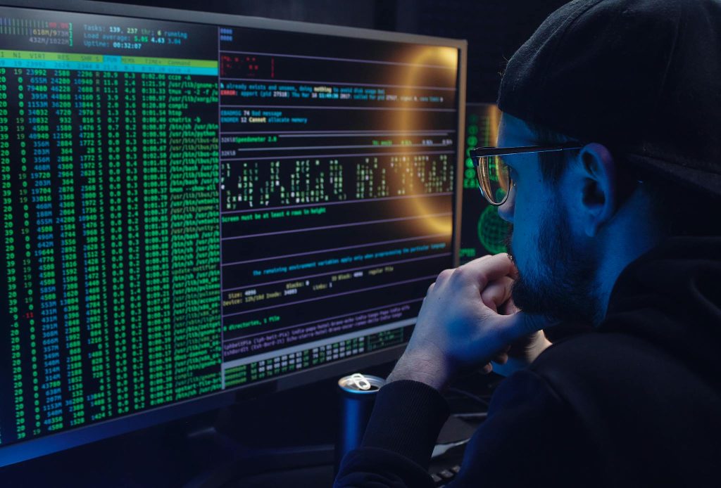 Man intently working on computer programming with code displayed on dual monitors in a dimly lit room.